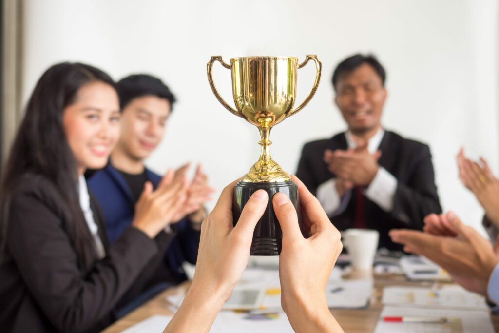 a person holding up a trophy - other colleagues cheering for the person - total office environment 
